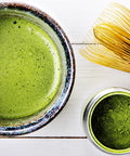 Matcha Tee im Schälchen und in Tasse, Bambusbesen auf Holz
