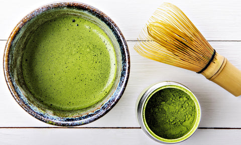 Matcha Tee im Schälchen und in Tasse, Bambusbesen auf Holz